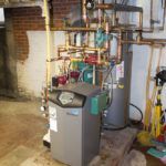 A boiler is sitting in a basement next to a water heater.