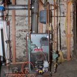A boiler is sitting in a basement next to a wall.