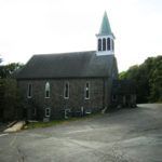 A small church with a steeple in the middle of a parking lot.