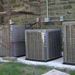 Two air conditioners are sitting next to each other in front of a brick building.