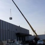 A crane is lifting a large object in the air in front of a building.