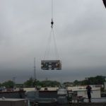 A crane is lifting an air conditioner from the roof of a building.