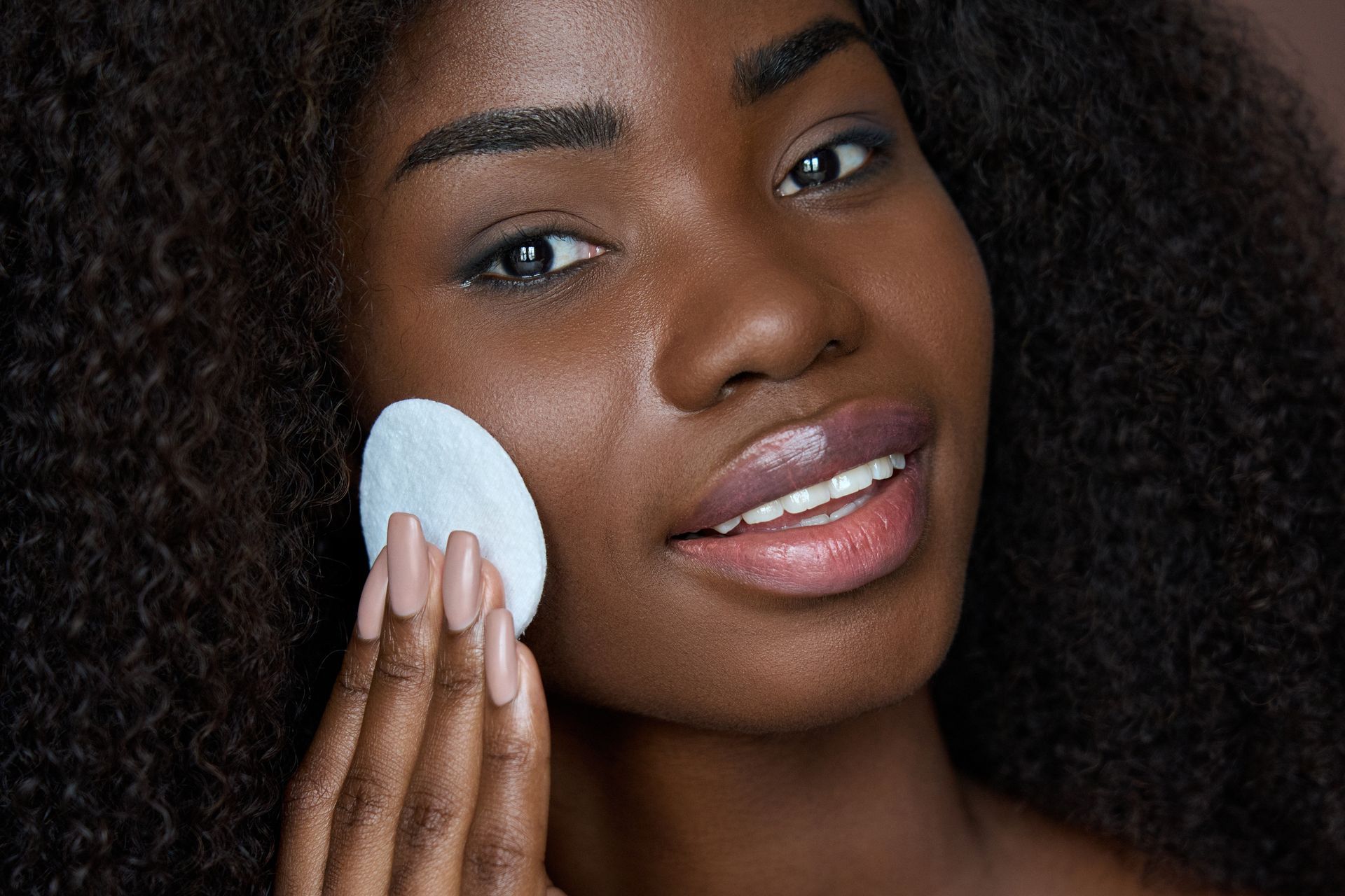 A woman is cleaning her face with a cotton pad.