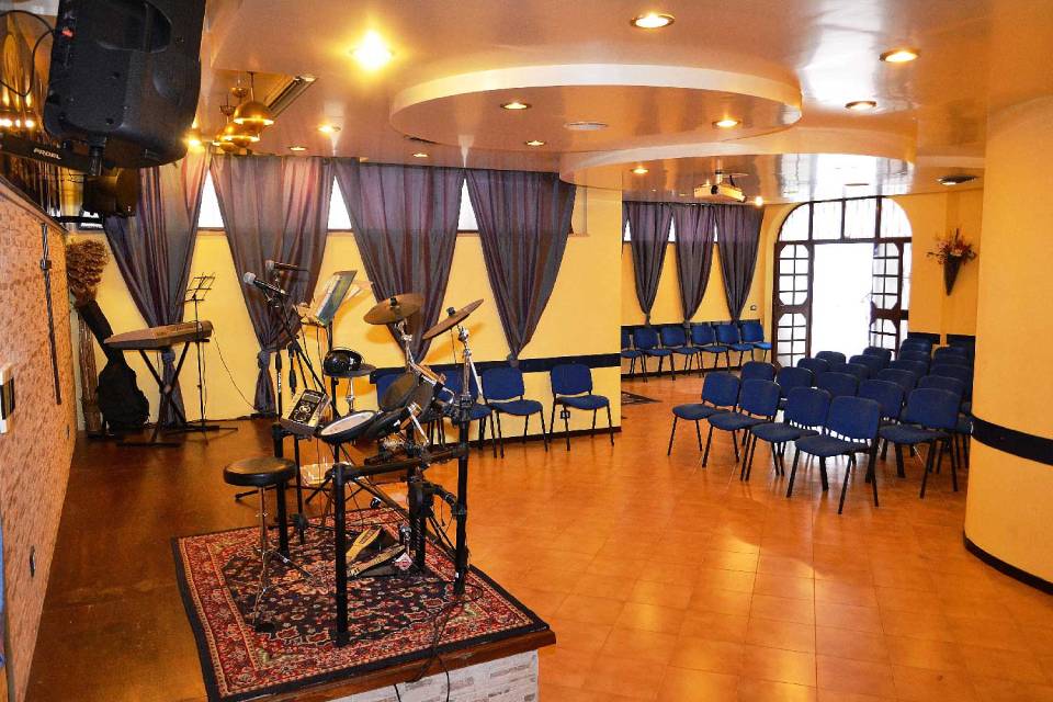 sala con posti a sedere e palco con batteria