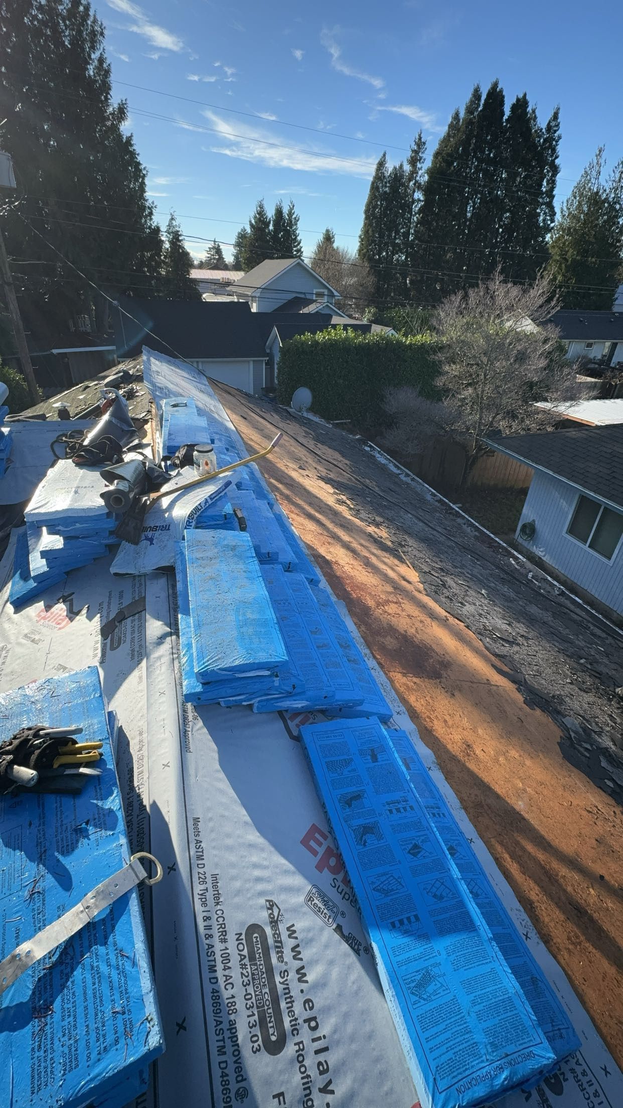 The roof of a house is being covered in blue tarps.