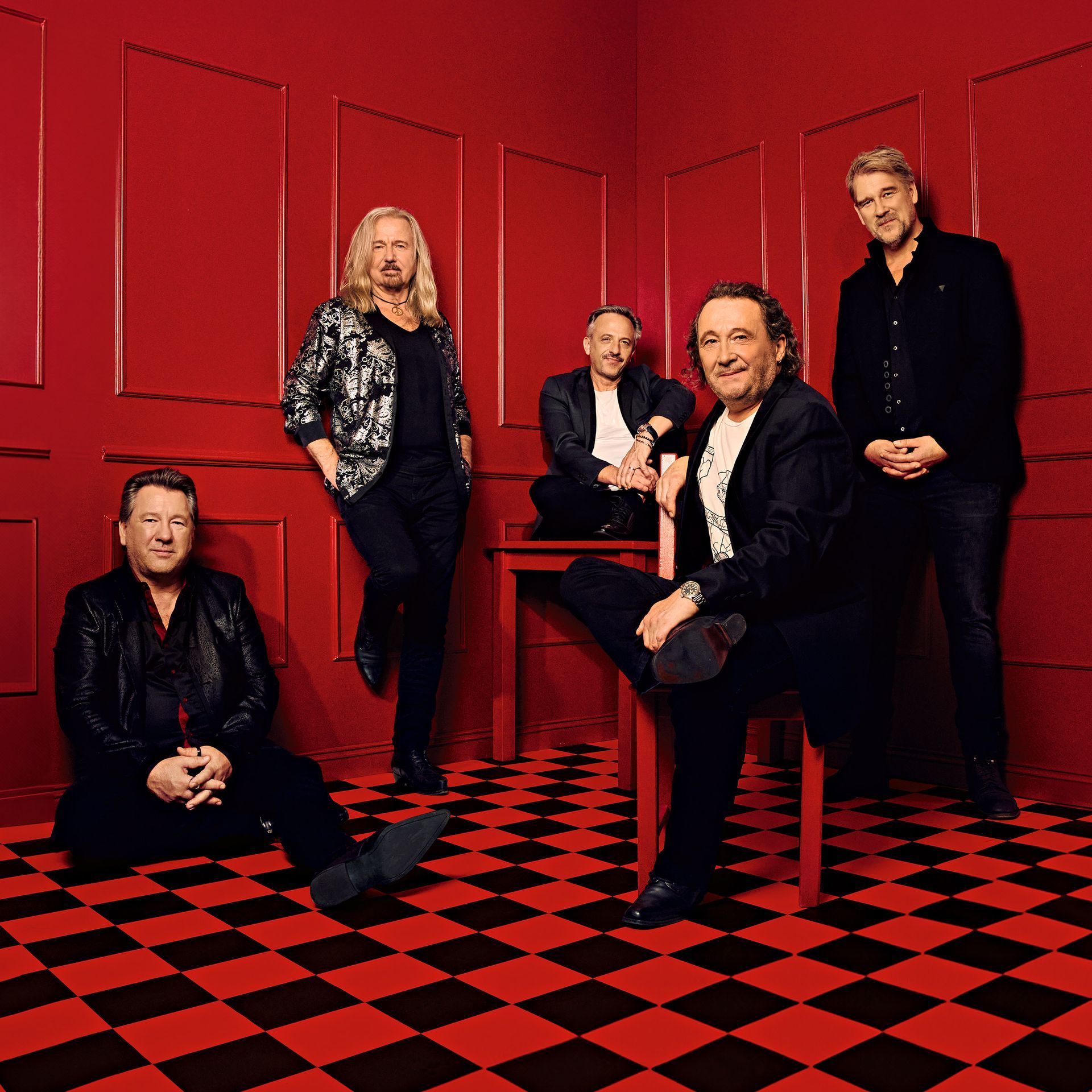 De fünf Mitglieder der Band KARAT in schwarzen Anzügen in einem roten Raum