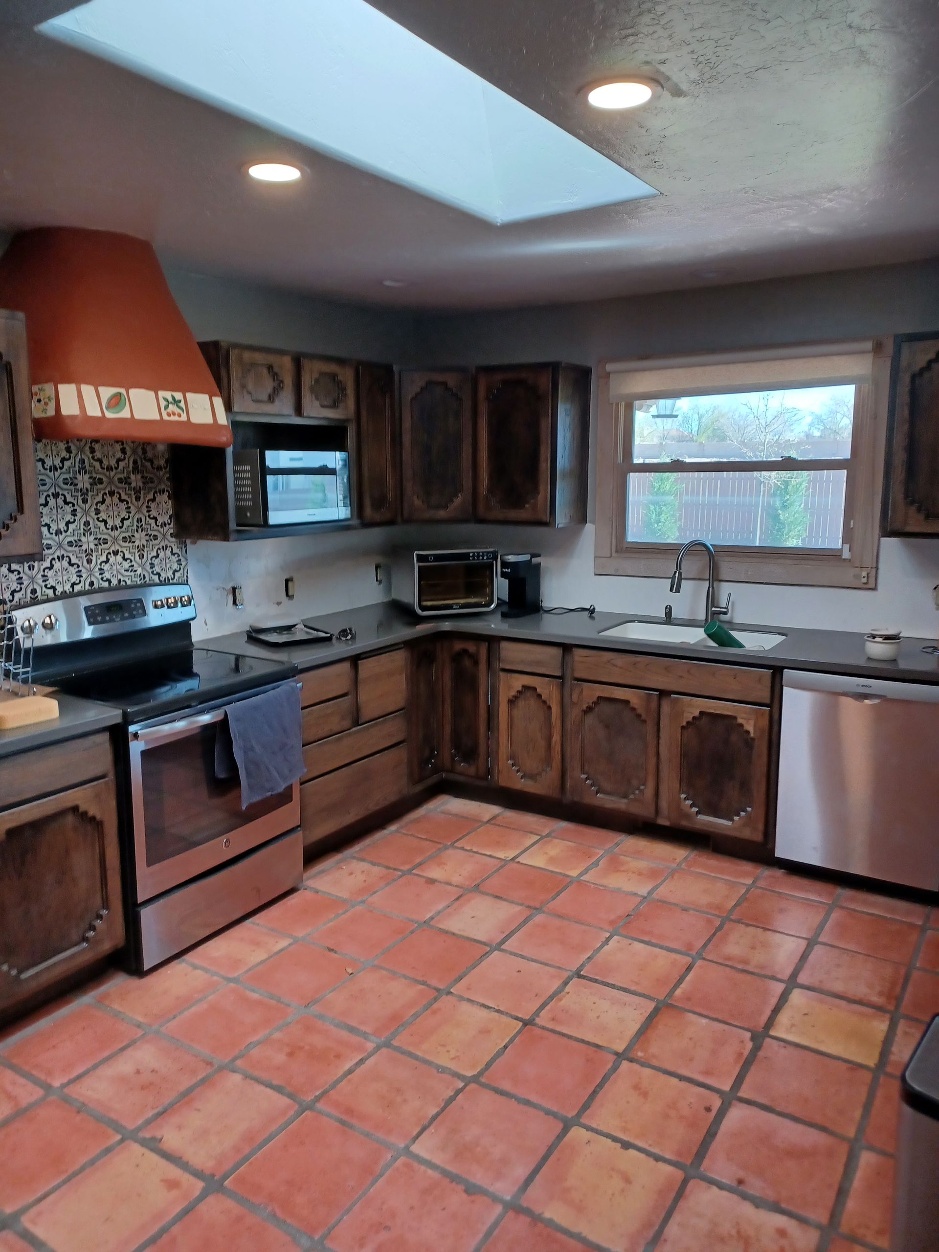 Kitchen with brown cabinets, terracotta tile floor, stainless steel appliances, and a skylight.