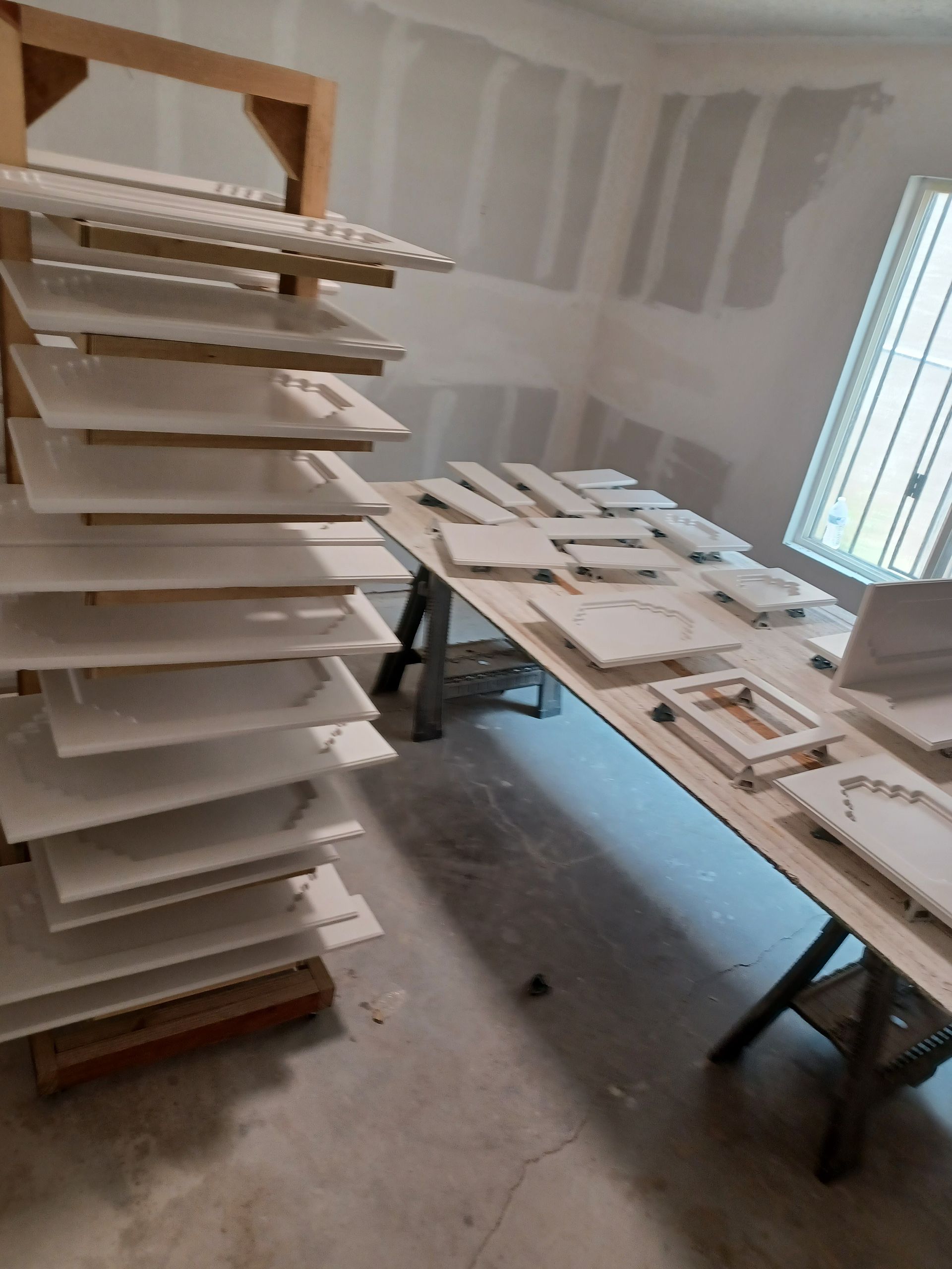 White plaster art pieces drying on shelves and a table in a room with unfinished walls.