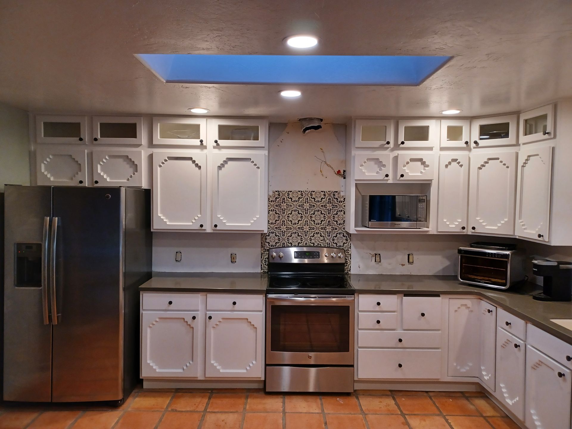 Kitchen with white cabinets, stainless steel appliances, brown countertops, and a skylight.