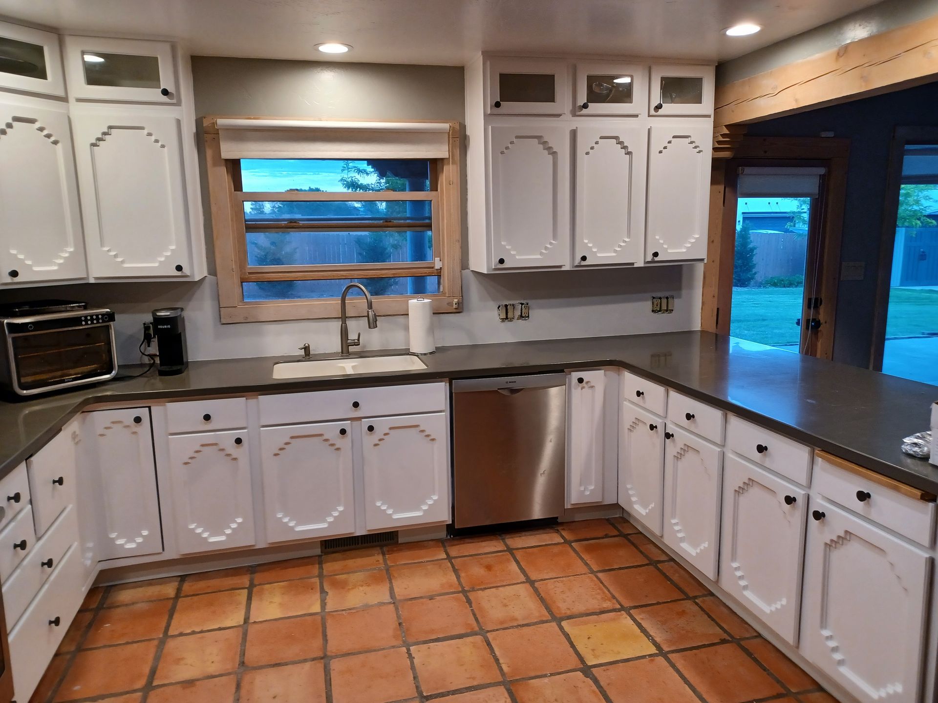 White kitchen with dark countertops, stainless steel appliances, and terracotta tile floors.