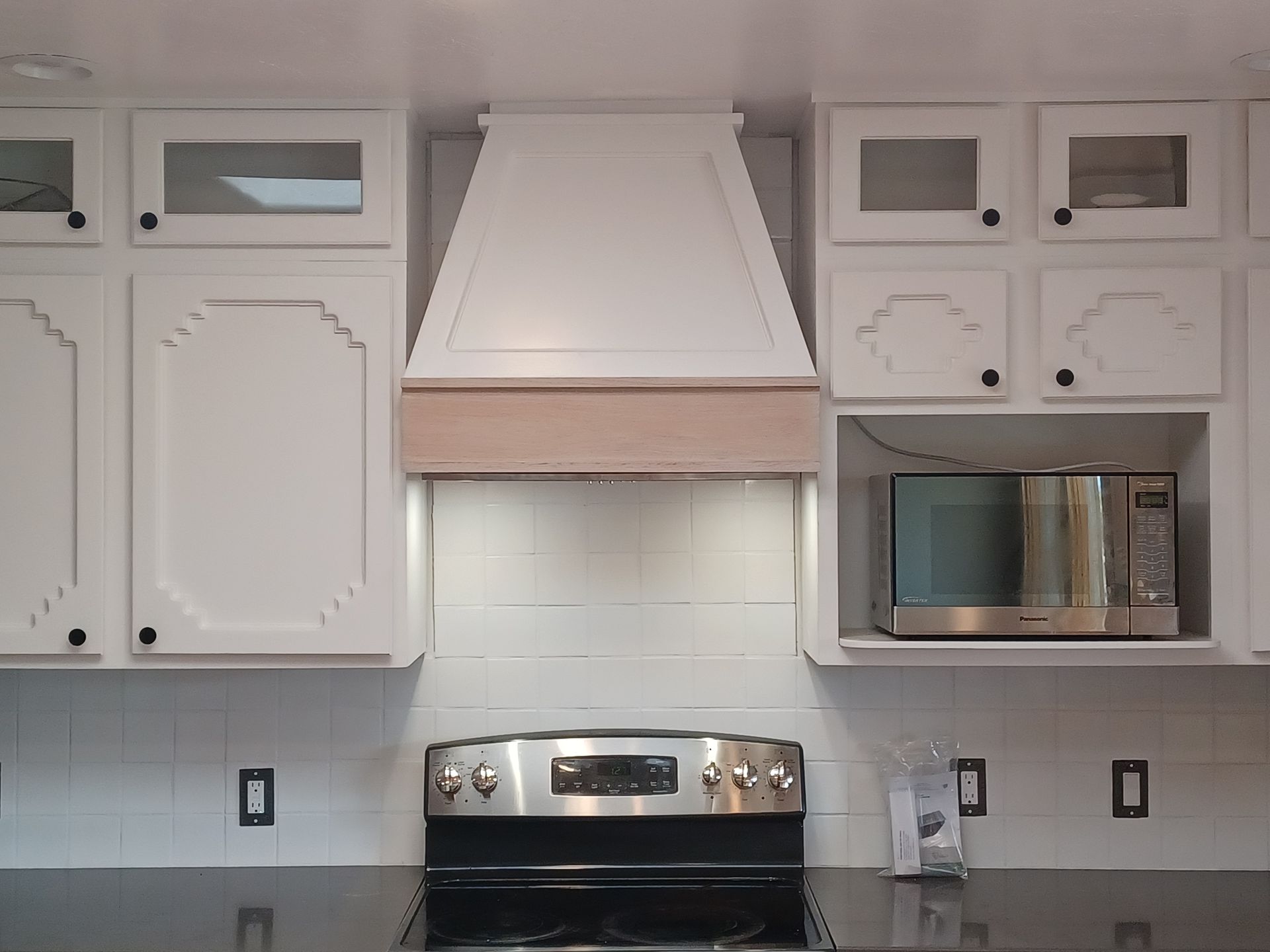 White kitchen cabinets with range hood above a stainless steel stove, with a microwave and black countertops.