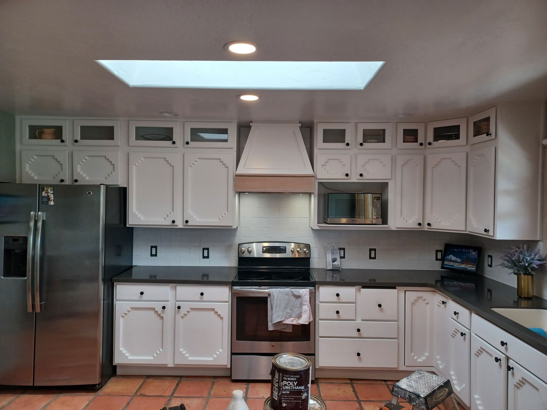 White kitchen with stainless steel appliances, black countertops, and a skylight.