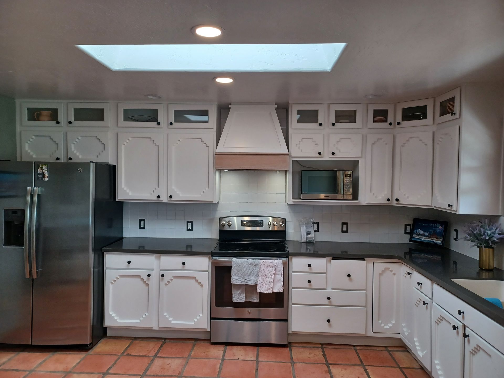 White kitchen with stainless steel appliances, dark countertops, and a skylight.
