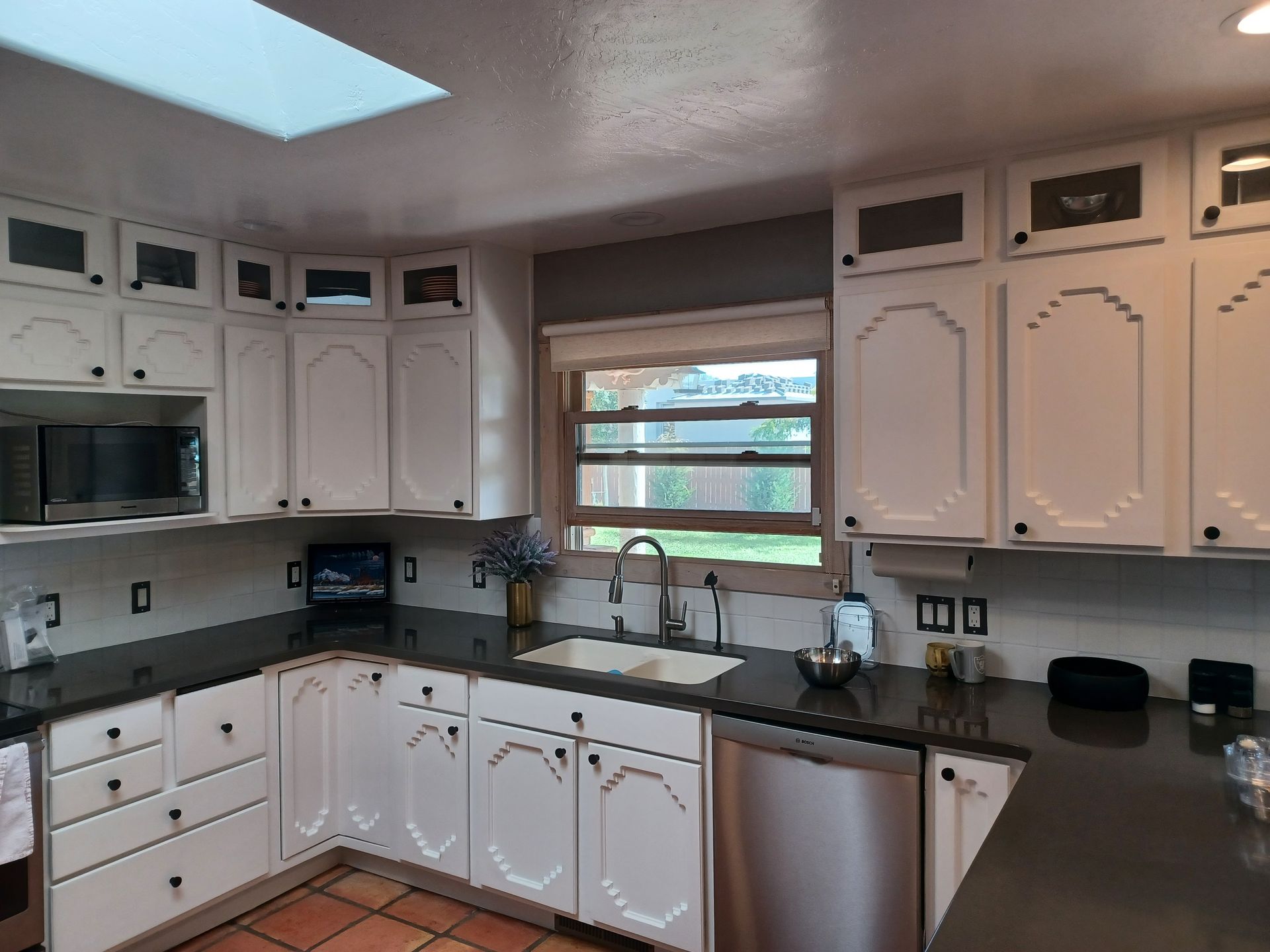 White kitchen cabinets with dark countertops, a stainless steel dishwasher, and a window.