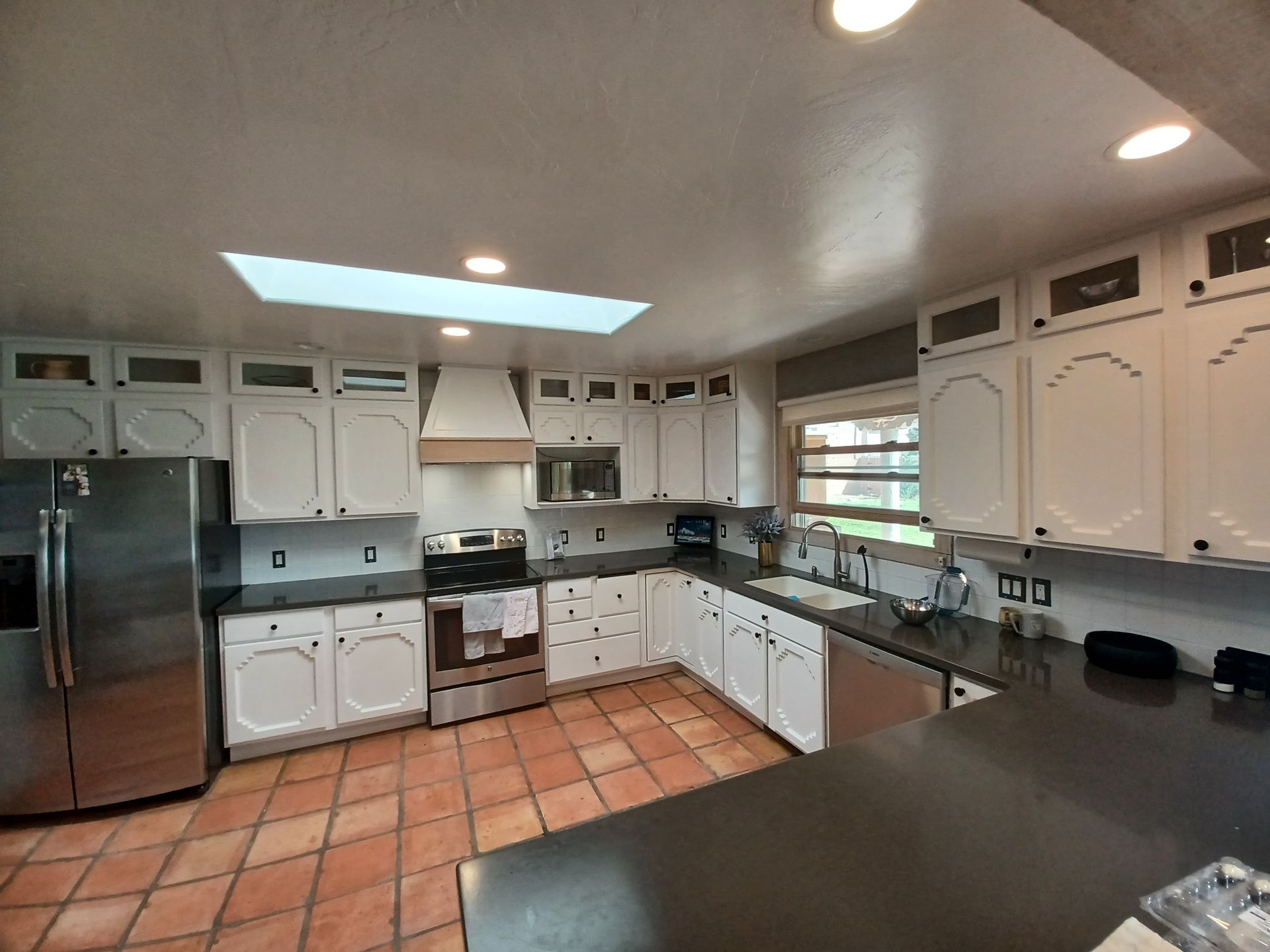 White kitchen with stainless steel appliances, black countertops, and a terracotta tile floor.