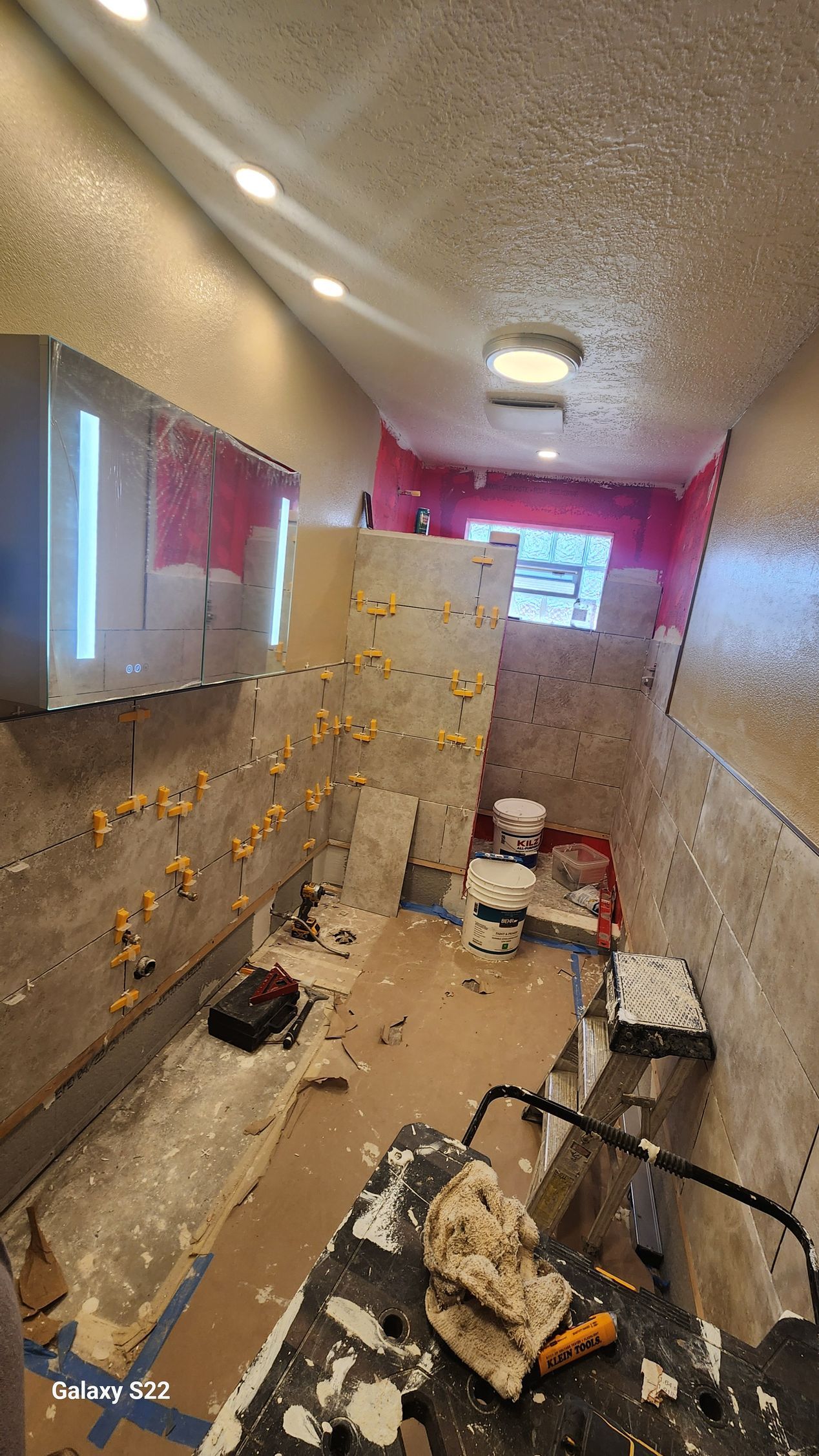 Bathroom under renovation with tile, tools, and pink wall.
