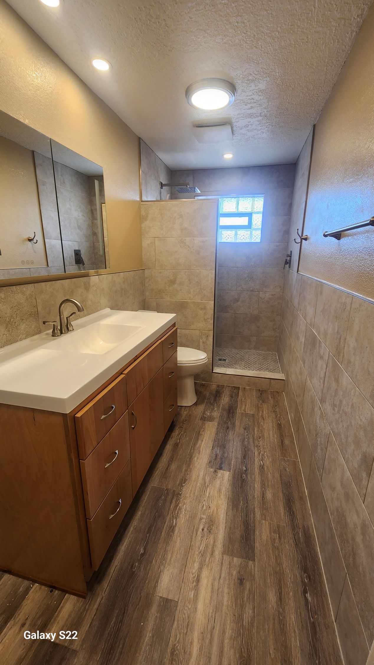 Bathroom with wooden vanity, tiled shower, and wood-look flooring.