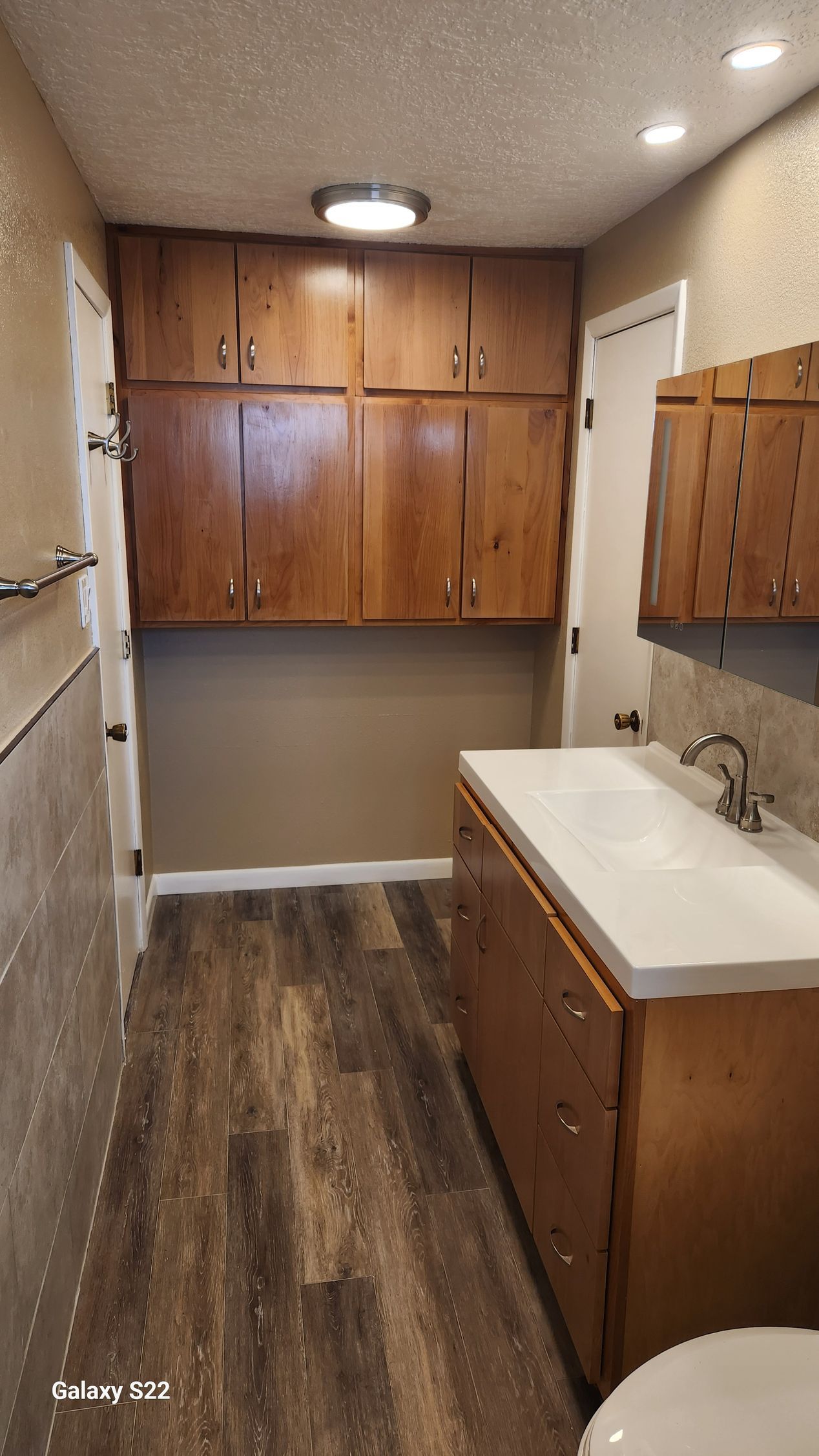 Bathroom with wood cabinets, sink, toilet, and wooden-look flooring.