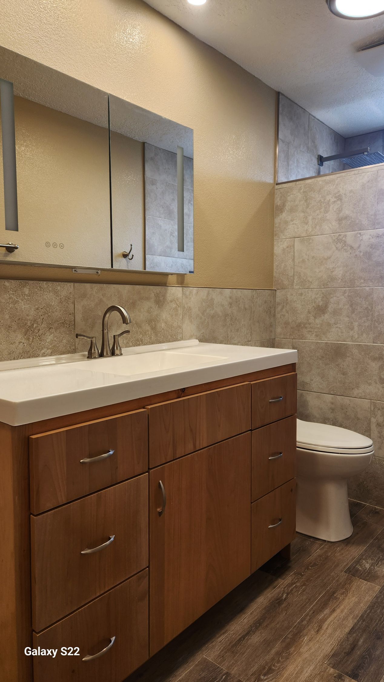 Bathroom with wooden vanity, tan walls, and tile shower. White countertop, sink, and toilet visible.