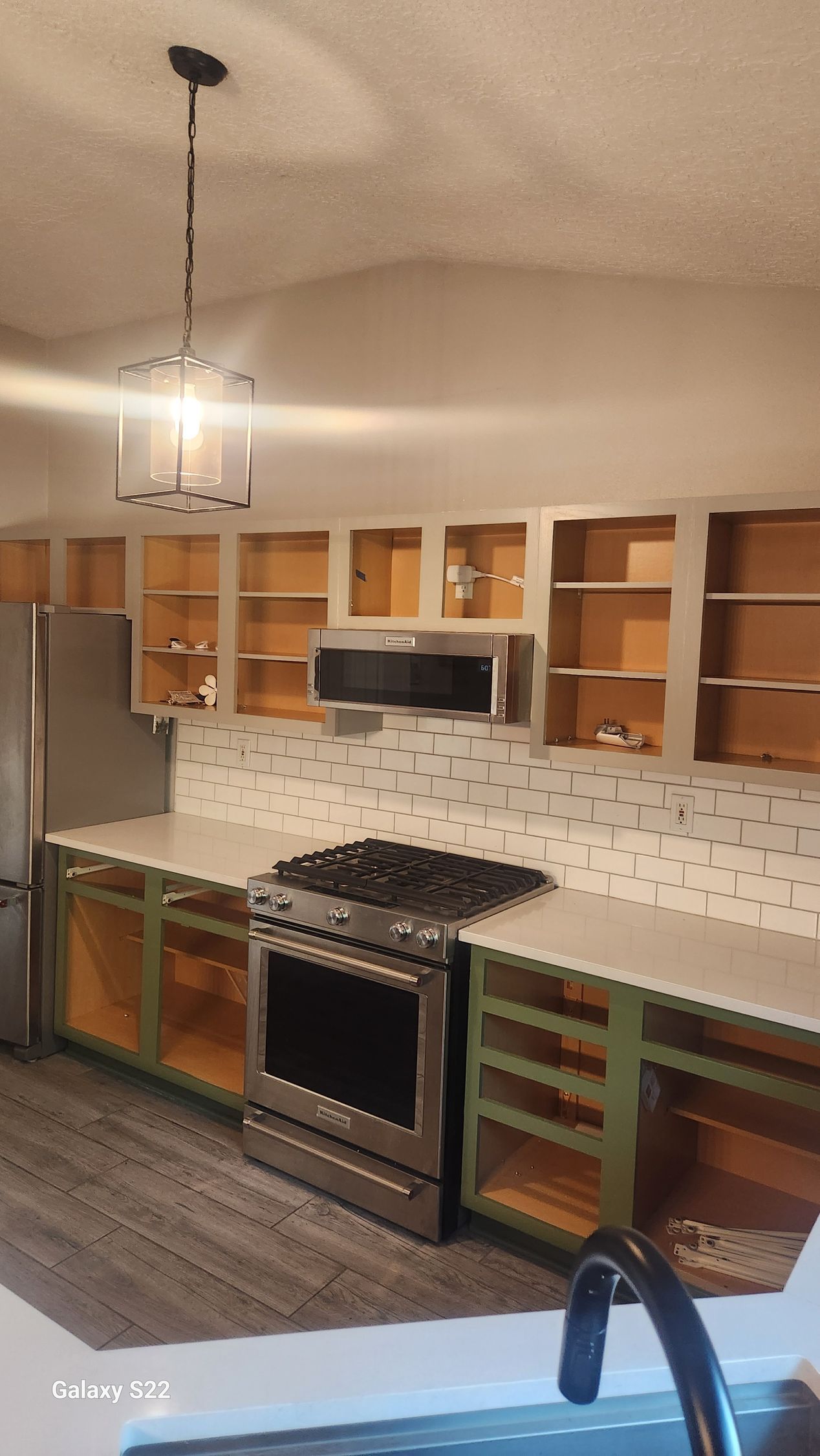 Kitchen under renovation; cabinets with green and wood tones, stainless steel stove, tile backsplash, and white countertop.