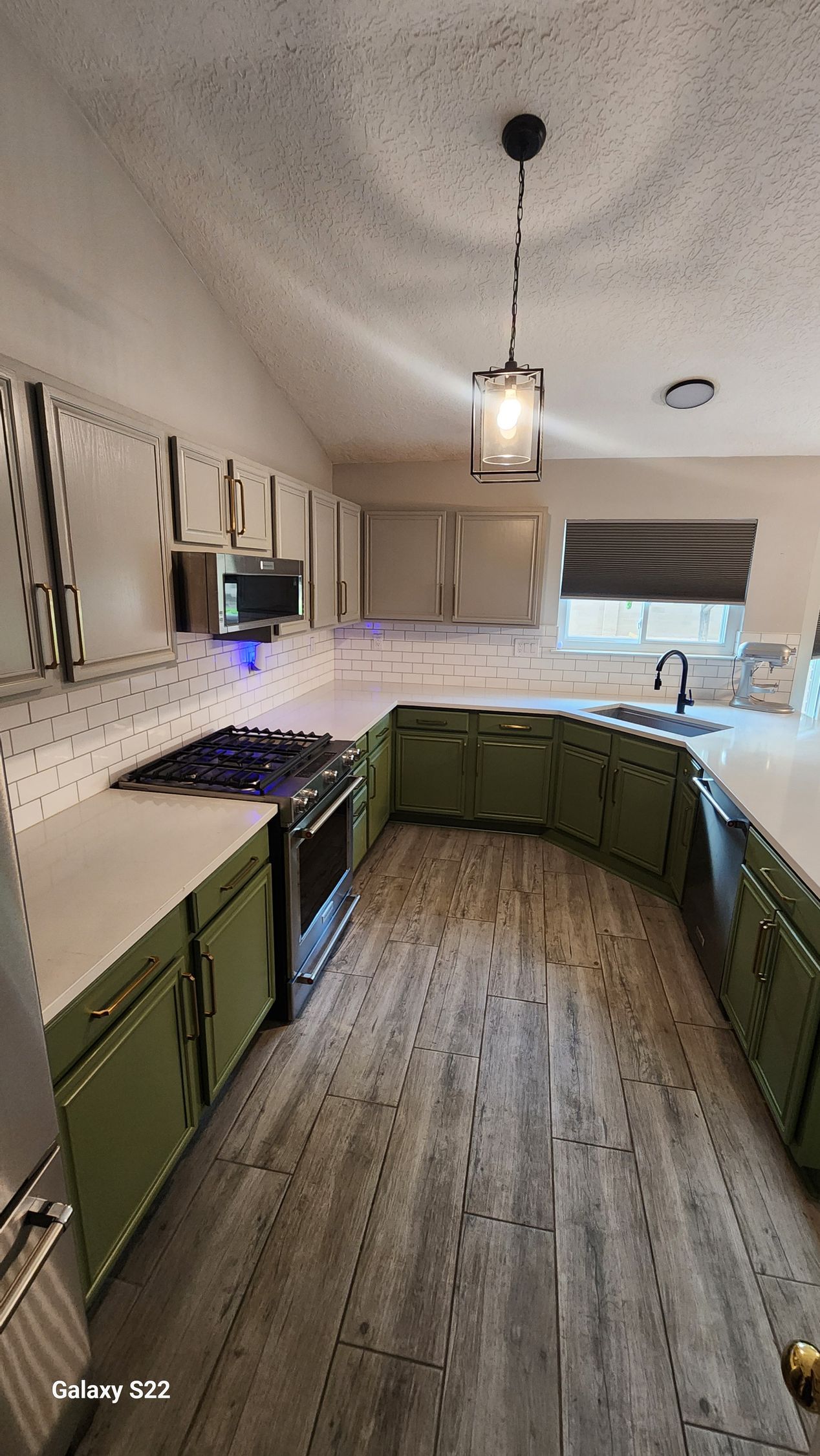 Kitchen with green cabinets, white countertops, and a pendant light.