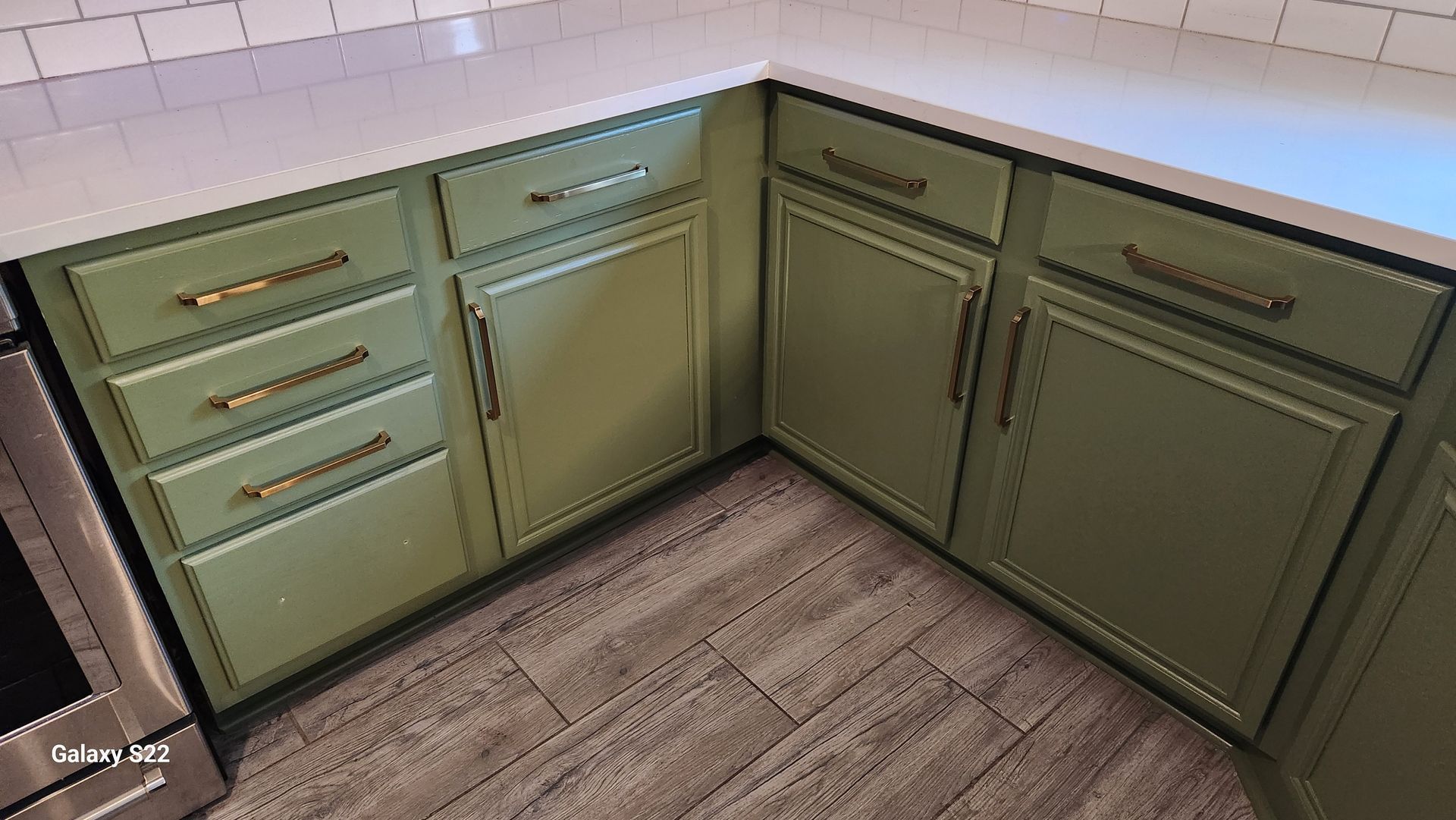 Green kitchen cabinets with brass hardware and white countertops.