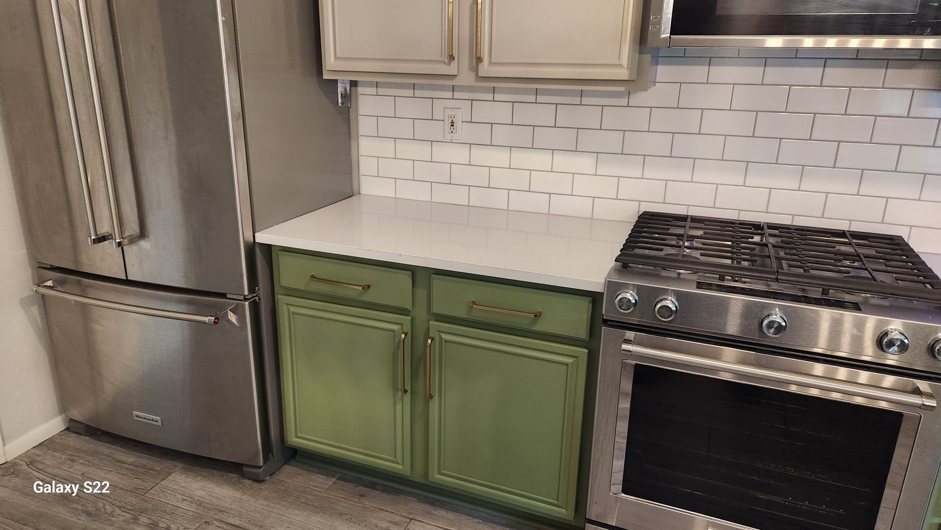 Stainless steel appliances with green cabinets, white countertop, and white subway tile backsplash.