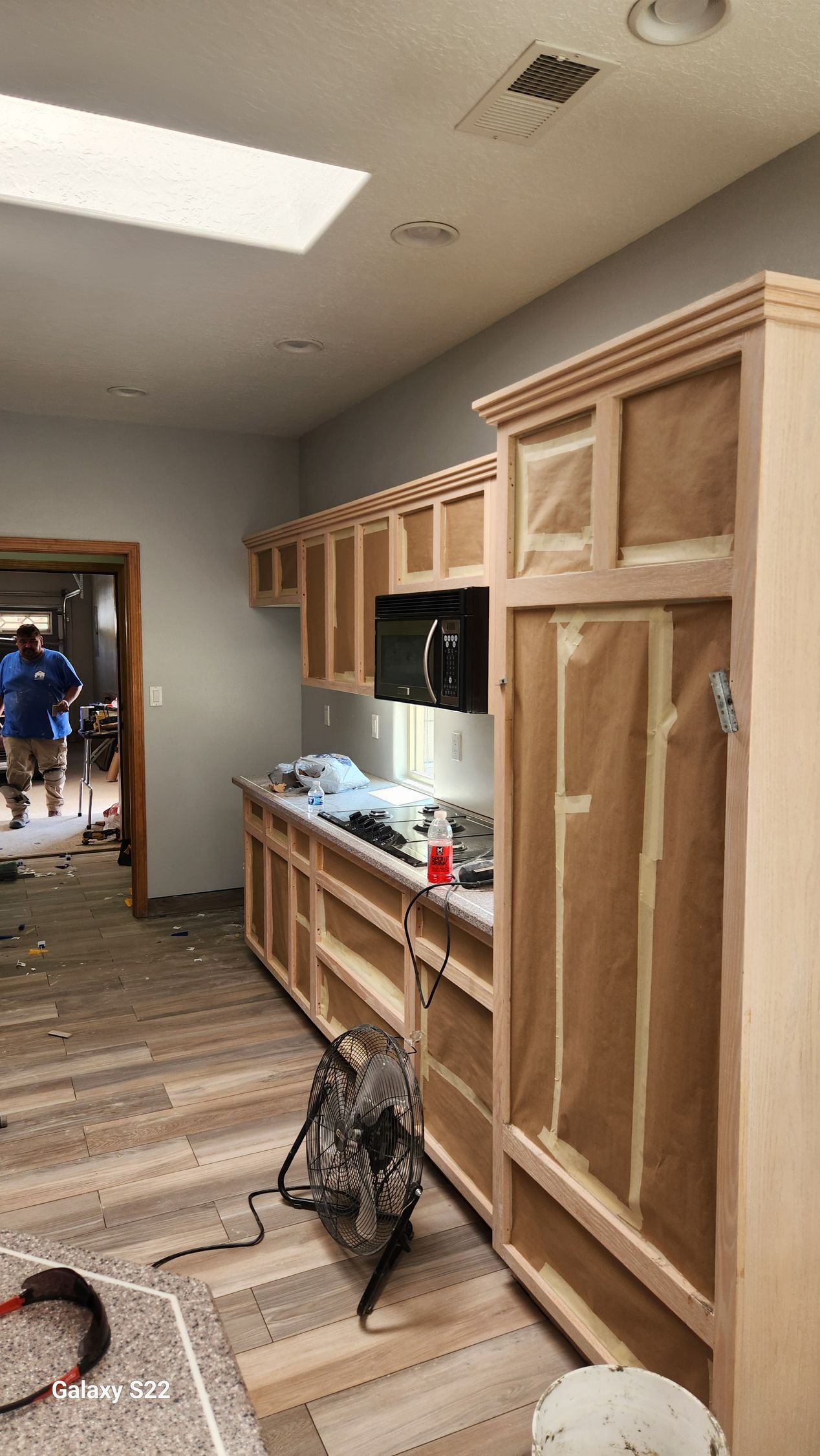 Kitchen under construction, cabinets covered in paper, tools on floor, person in doorway.