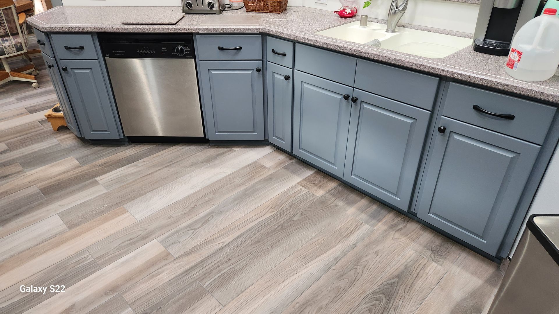 Blue kitchen cabinets and stainless steel appliances in a room with wood-look flooring.