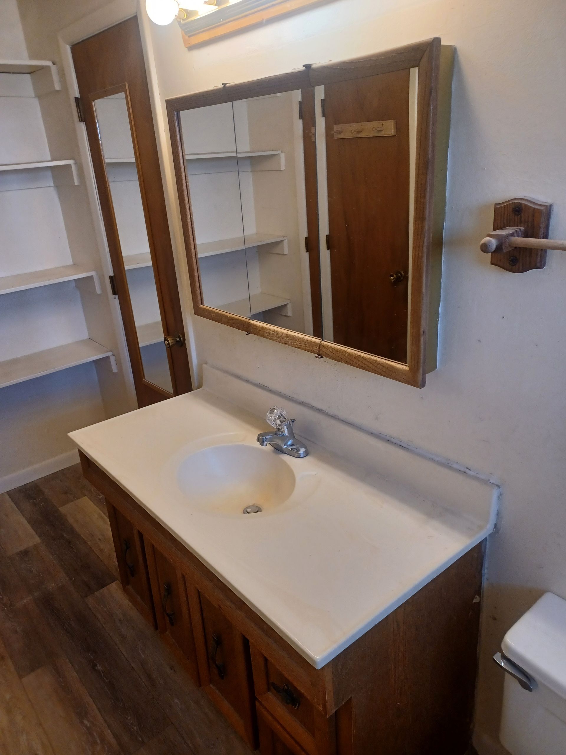 Bathroom with wooden vanity, sink, mirror, and a shelf unit to the left.