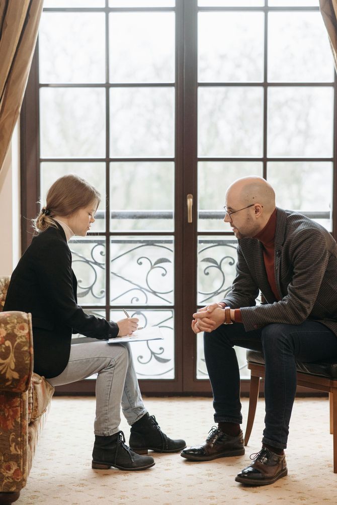 A man and a woman are sitting on a couch talking to each other.