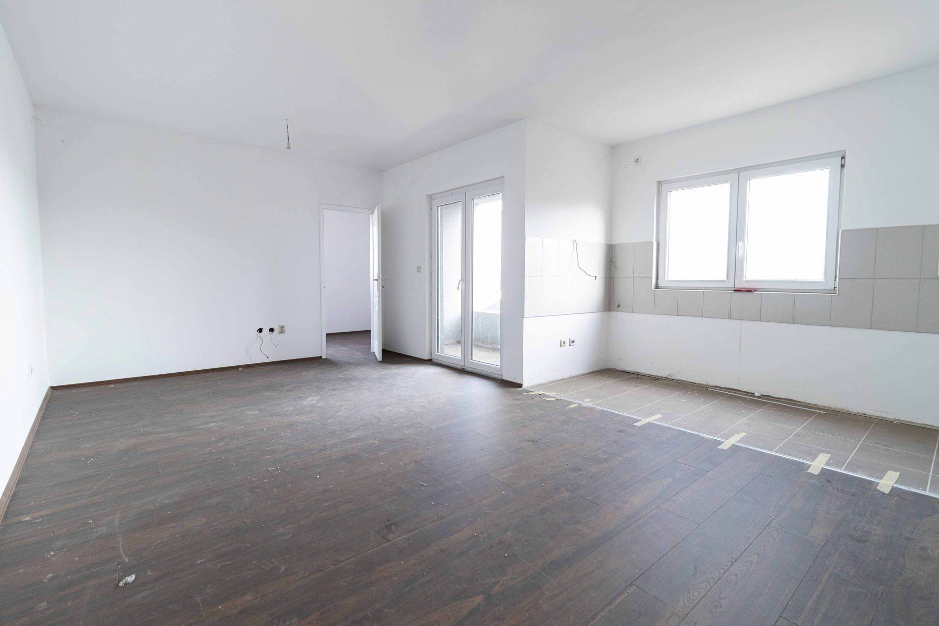 Empty room with dark wood flooring, white walls, and a window.