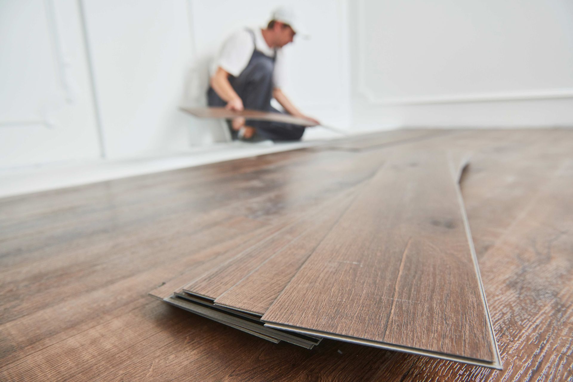 Man installing wood flooring in a room. Boards are brown; walls are white.