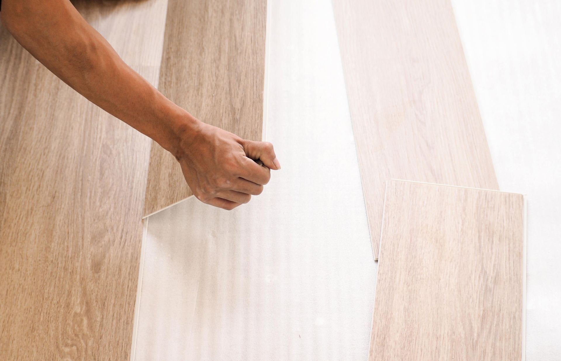 Person installing light-colored wood flooring; hand holding and positioning a plank.