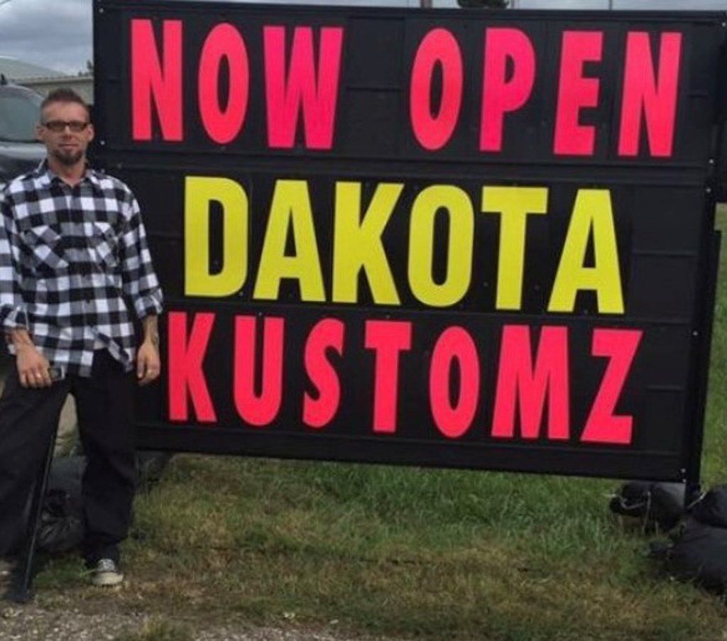 owner travis posing in front of now open dakota kustomz sign
