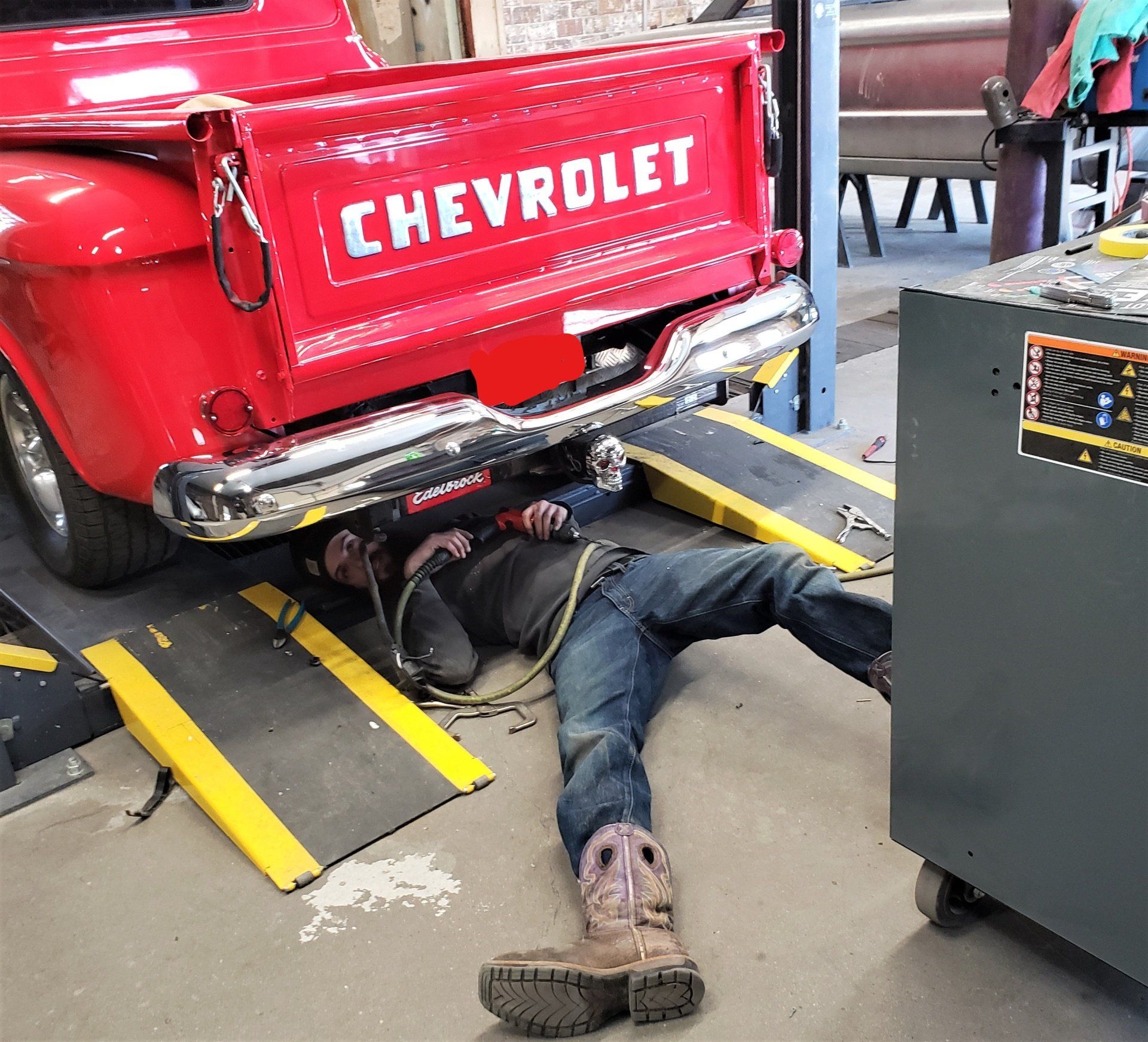 Dakota Kustomz worker doing maintenance under classic custom red ford pickup truck