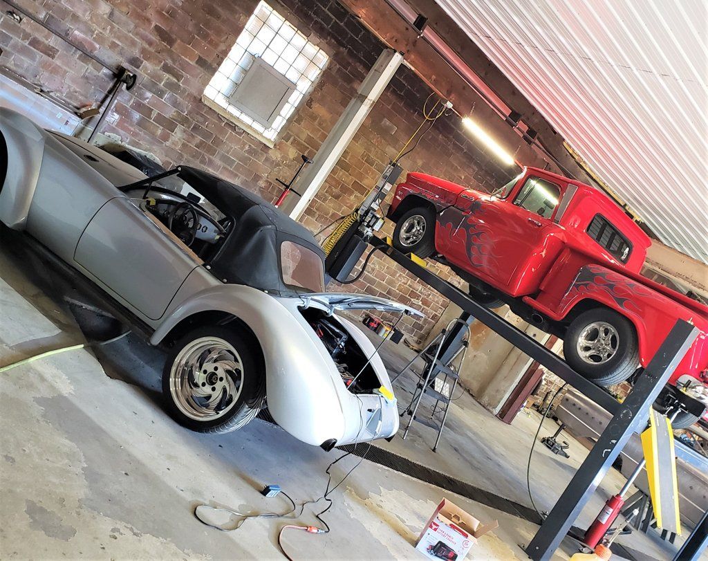 1962 customized red truck with grey flames suspended on service bay with another hot rod in the garage