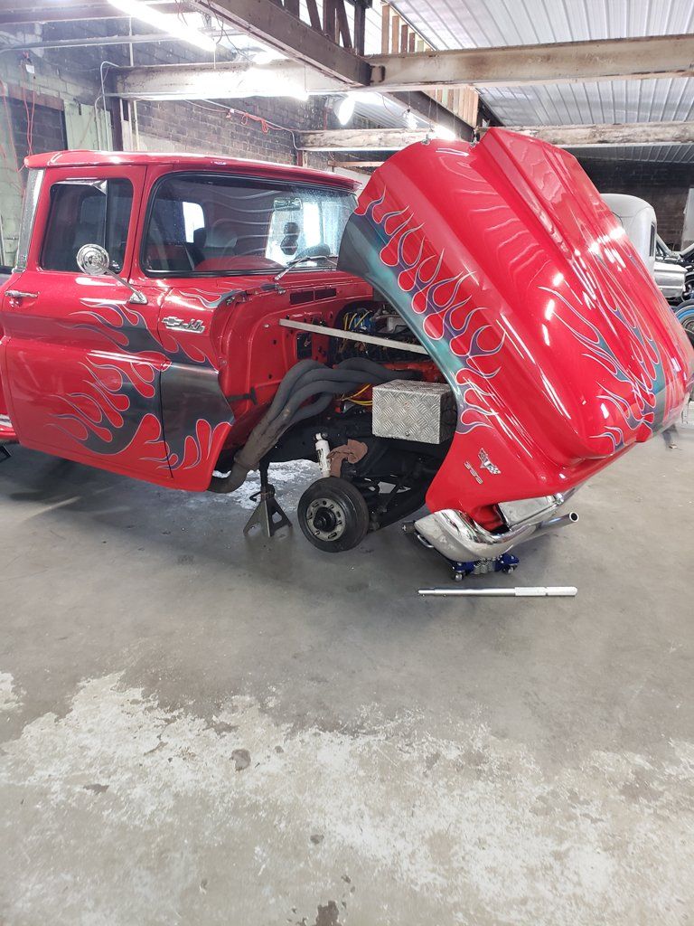 side view of 1962 red customized truck with grey flames with hood open and wheels removed
