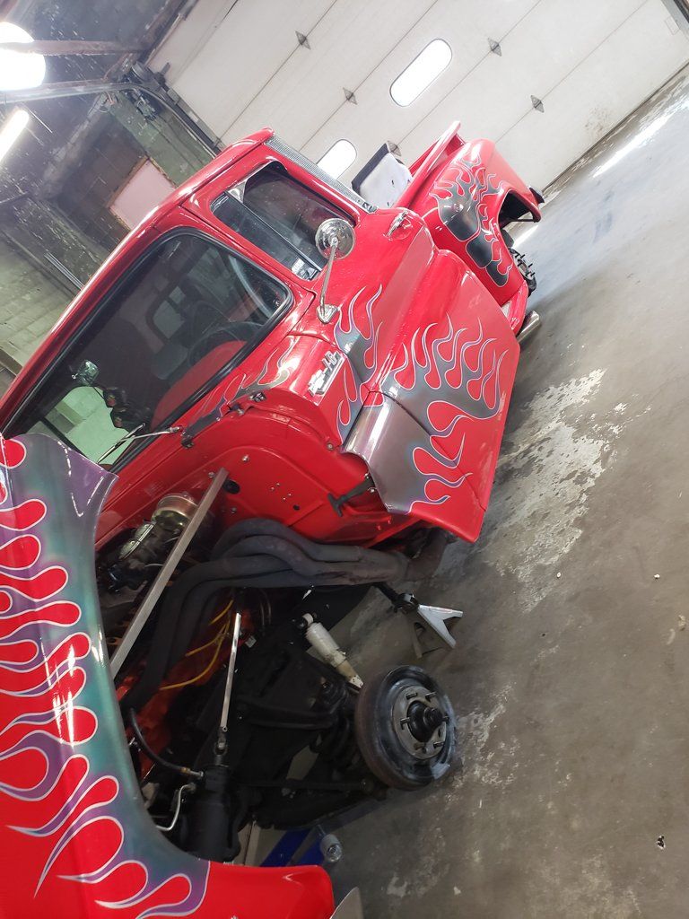 front side view of 1962 red customized truck with grey flames with wheels removed and hood open