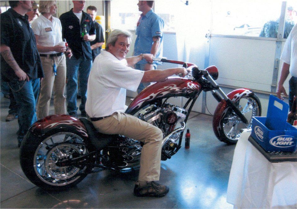 older gentleman sitting on customized chopper with crowd around him