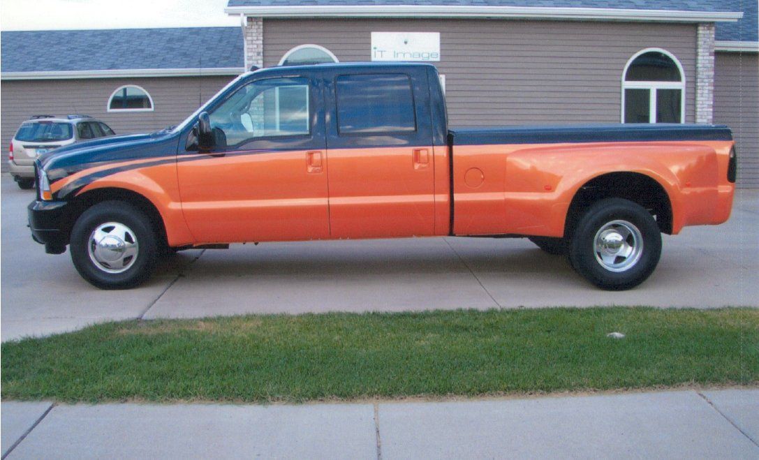 side profile view of orange and black customized pickup truck next to grass and sidewalk
