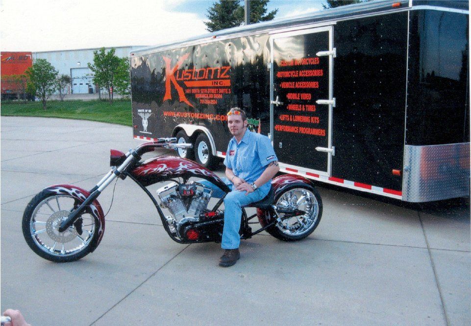 man in labor uniform sitting on chopper in front of kustomz inc trailer