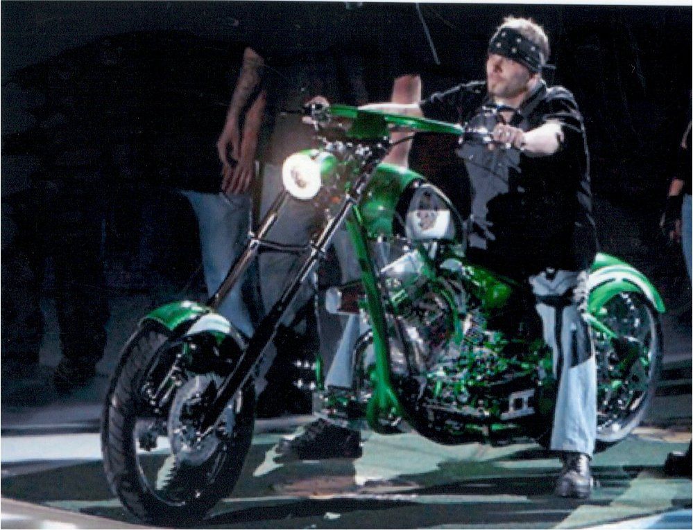 rider riding customized green chopper indoors with headlight on