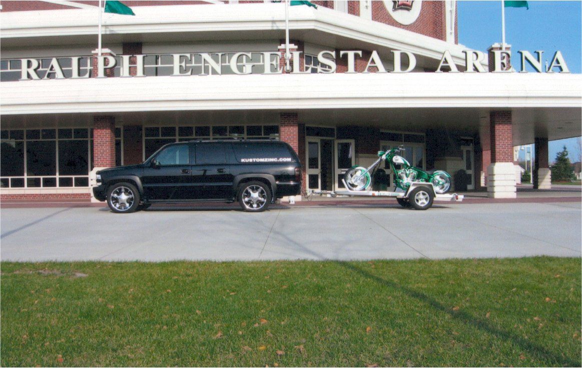 chopper on flatbed trailer pulled by black suv in front of englestad