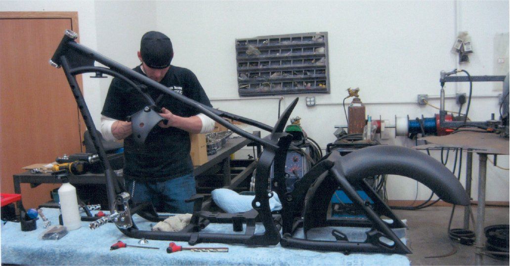 mechanic working on detailing chopper parts with chopper frame painted black on workbench