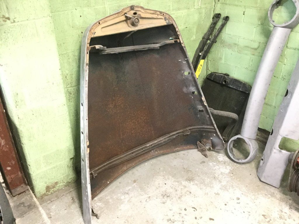 truck hood with rusting underneath leaning against green wall
