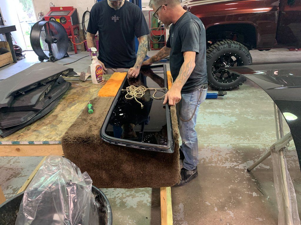 mechanics working on rear windshield on workbench