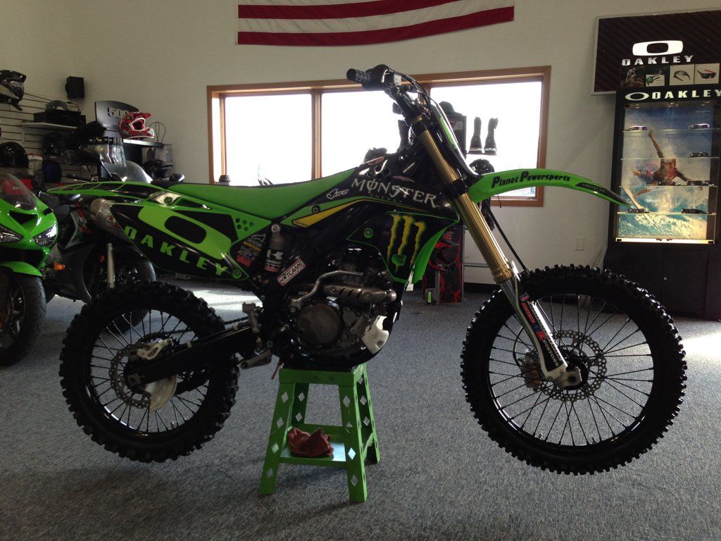 darker right side view of custom black and lime green bike with monster energy drink and oakley logo indoors with american flag in background