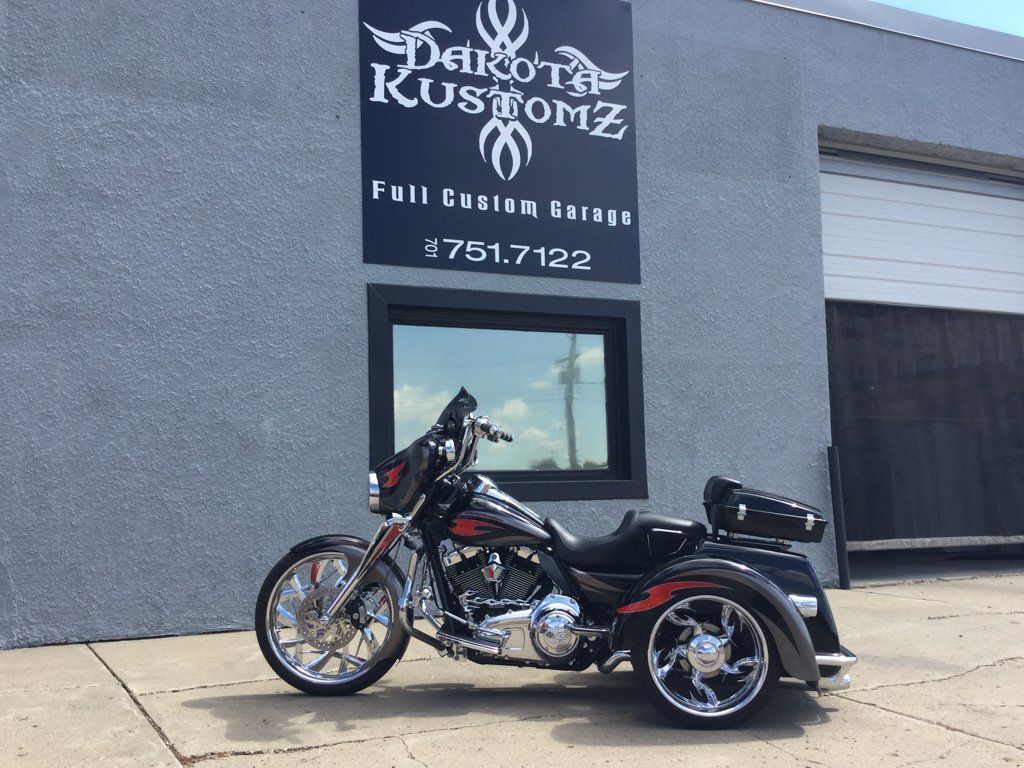 side view of customized black three wheel motorcycle  in front of dakota kustomz garage