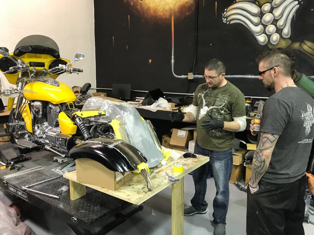 yellow motorcycle on service bay with two workers planning out customization